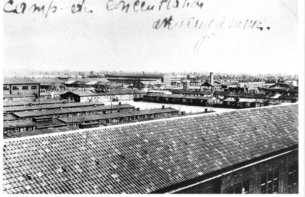 Aerial view, black and white photo: roof of a house in the foreground, prisoners' barracks and roll call square in the background.