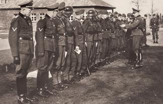 Black and whithe photo: Several SS men in uniform stand in a row. An officer stands in front of the row and awards medals.